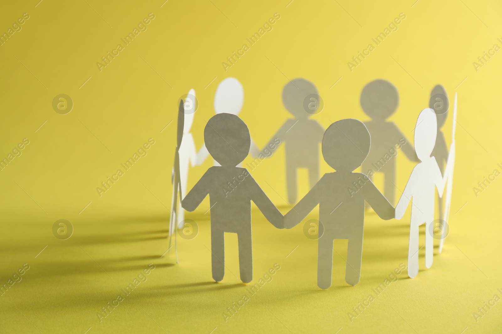 Photo of Teamwork concept. Paper figures of people holding hands on yellow background, closeup and space for text