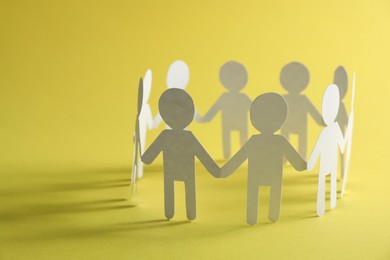 Photo of Teamwork concept. Paper figures of people holding hands on yellow background, closeup and space for text