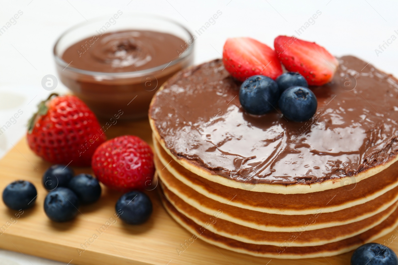 Photo of Tasty pancakes with chocolate paste and berries on table, closeup