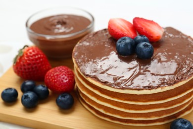 Photo of Tasty pancakes with chocolate paste and berries on table, closeup