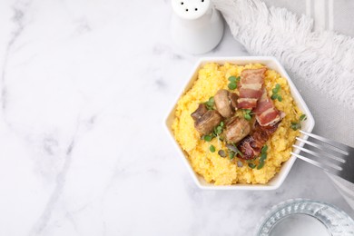 Photo of Cooked cornmeal with bacon, mushrooms and microgreens in bowl on white marble table, top view. Space for text