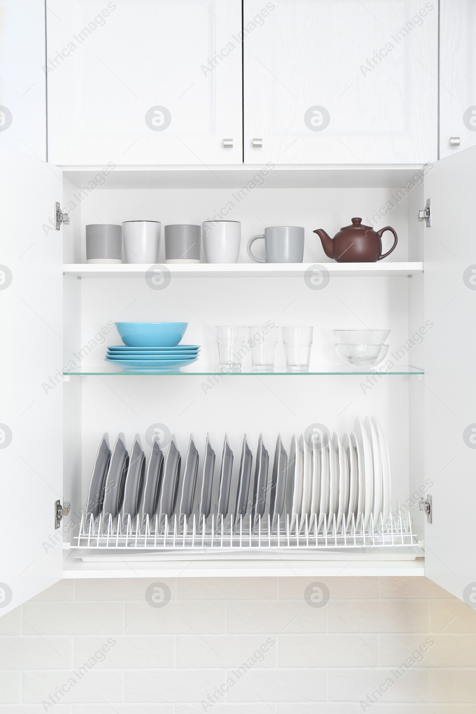 Photo of Open cabinet with different clean dishware in kitchen