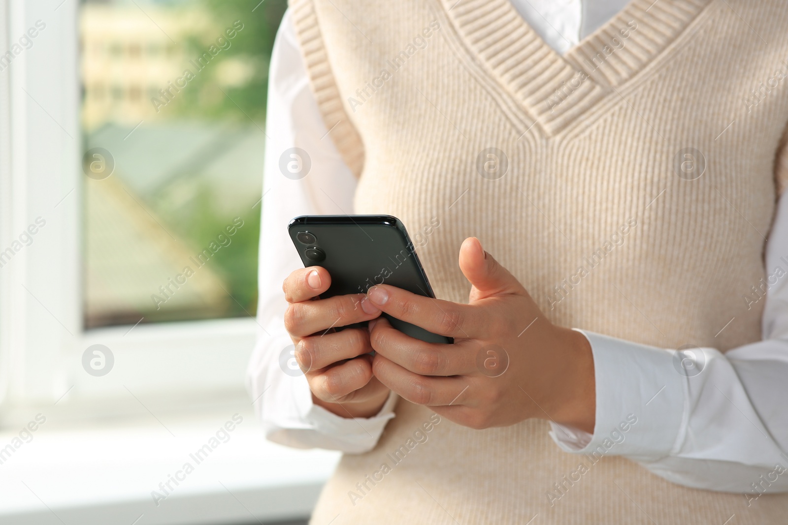 Photo of Woman using smartphone near window indoors, closeup