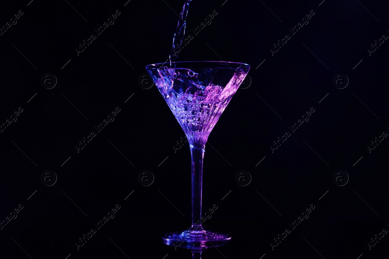 Photo of Pouring martini into glass in neon lights on dark background