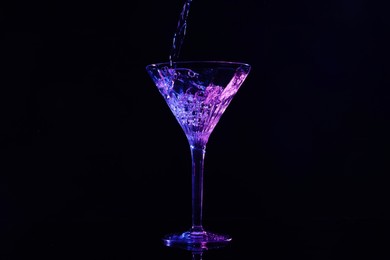 Photo of Pouring martini into glass in neon lights on dark background