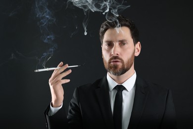 Man using long cigarette holder for smoking on black background
