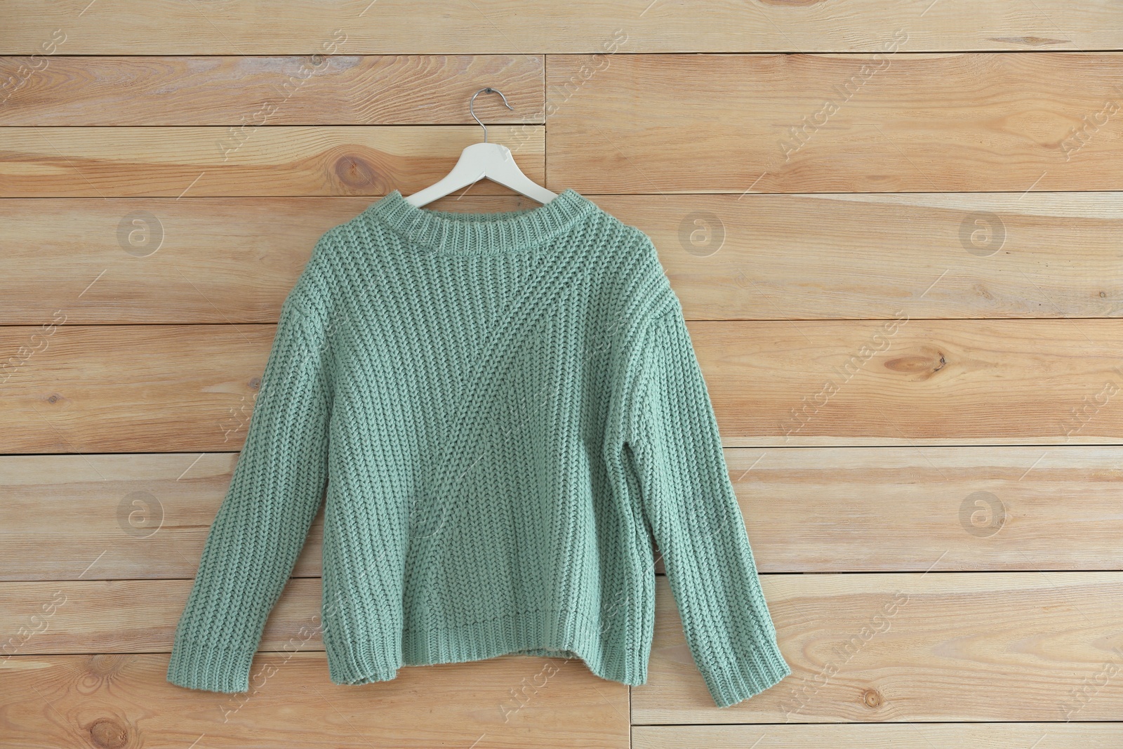 Photo of Hanger with stylish sweater on wooden wall