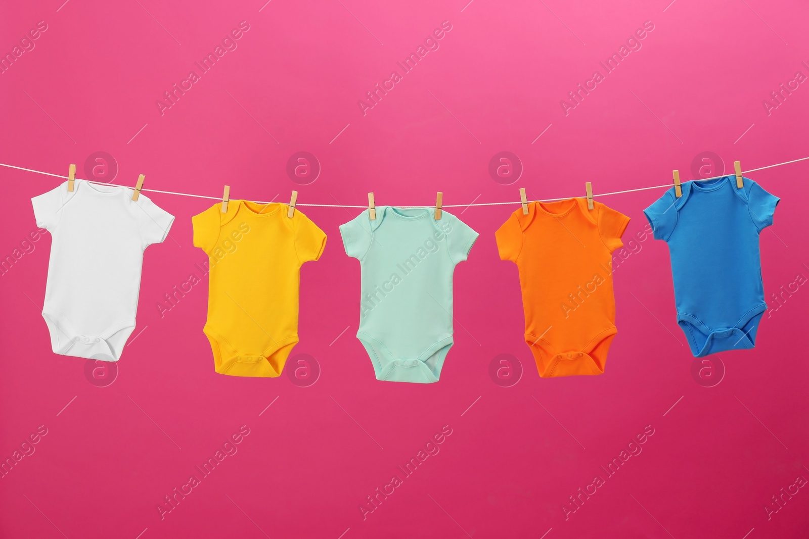 Photo of Baby onesies hanging on clothes line against pink background