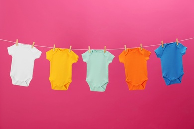 Photo of Baby onesies hanging on clothes line against pink background