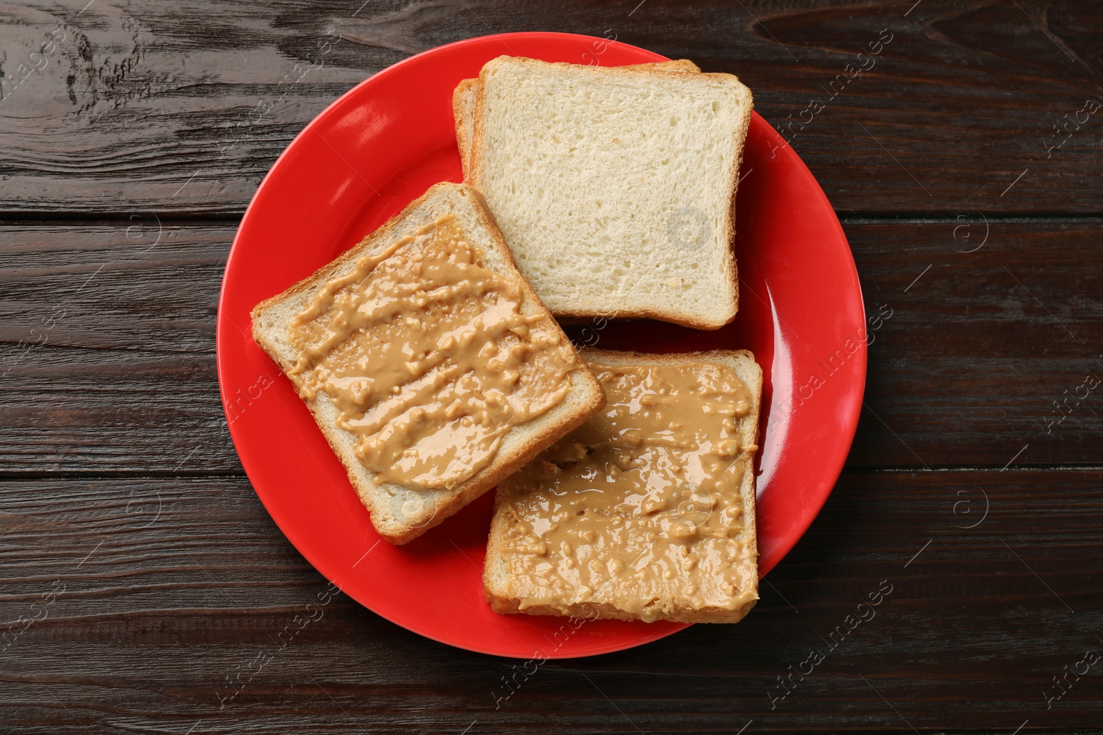 Photo of Delicious toasts with peanut butter on dark wooden table, top view