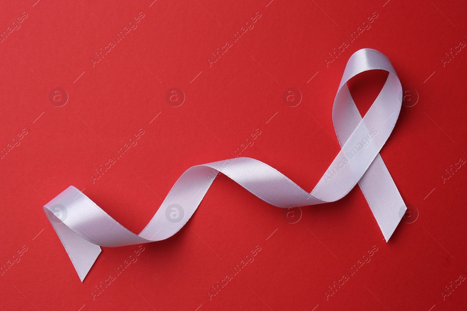 Photo of White awareness ribbon on red background, top view. Space for text