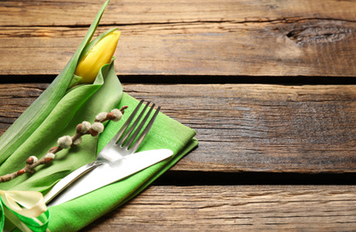 Photo of Cutlery set with beautiful willow branch and tulip on wooden table, space for text. Easter celebration