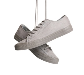 Pair of stylish sneakers hanging on white background