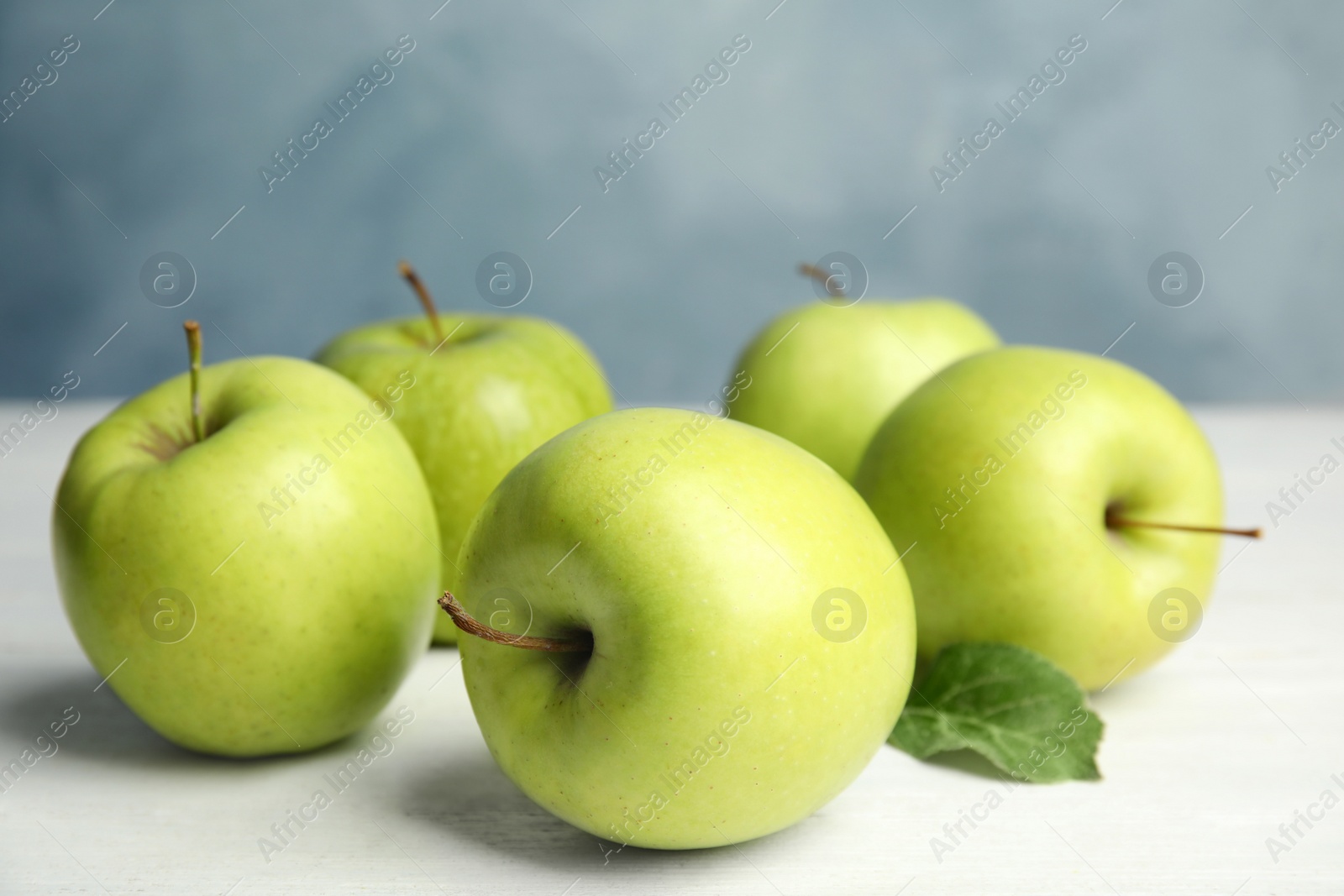 Photo of Fresh ripe green apples on white wooden table against blue background, space for text