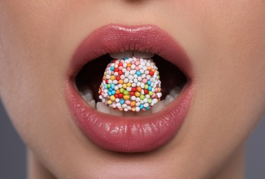 Woman with beautiful lips eating candy on grey background, closeup