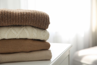 Photo of Stack of folded warm sweaters on white table indoors, closeup. Space for text