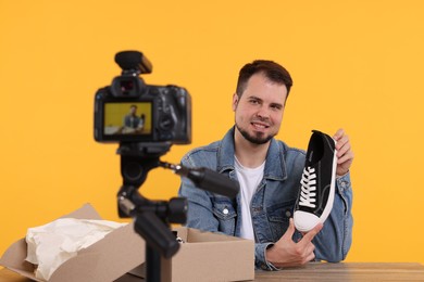 Smiling fashion blogger showing sneaker while recording video at table against orange background