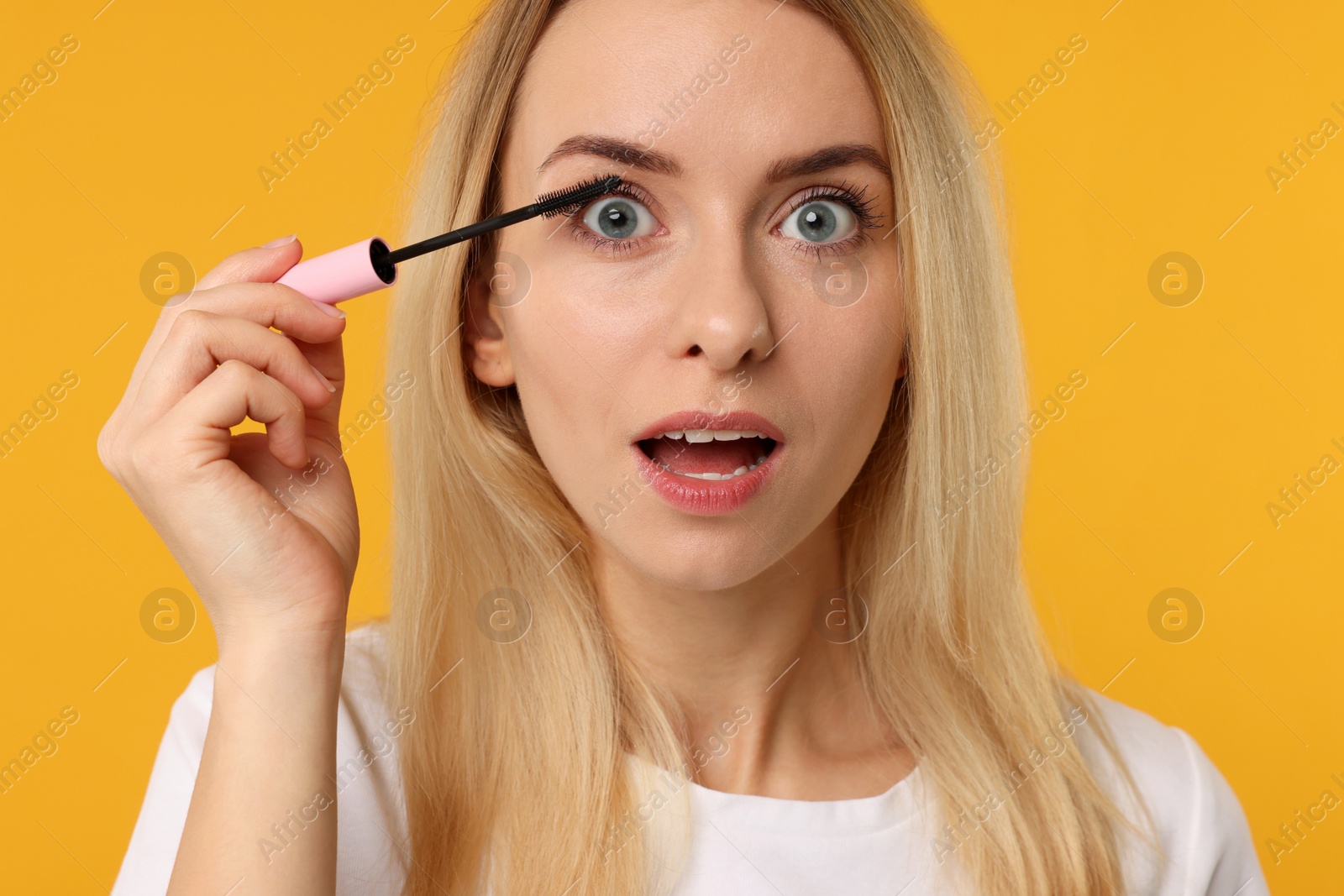 Photo of Beautiful woman applying mascara on orange background, closeup