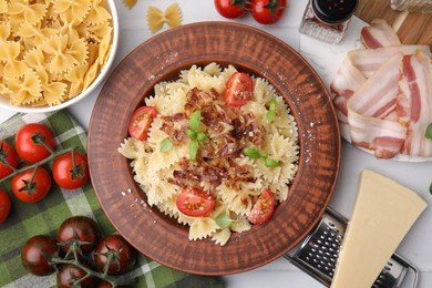 Photo of Tasty pasta with bacon, tomatoes and basil on white tiled table, flat lay