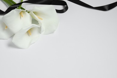 Photo of Beautiful calla lilies and black ribbon on white background, closeup with space for text. Funeral symbol
