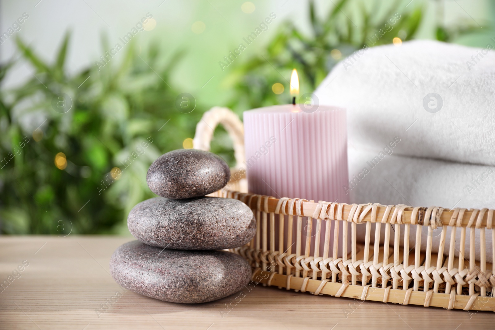 Photo of Spa stones and tray with towels and lit candle on wooden table, space for text