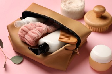Preparation for spa. Compact toiletry bag with different cosmetic products on pink background, closeup