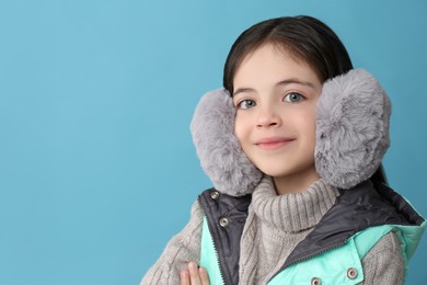 Cute little girl wearing stylish earmuffs on light blue background. Space for text