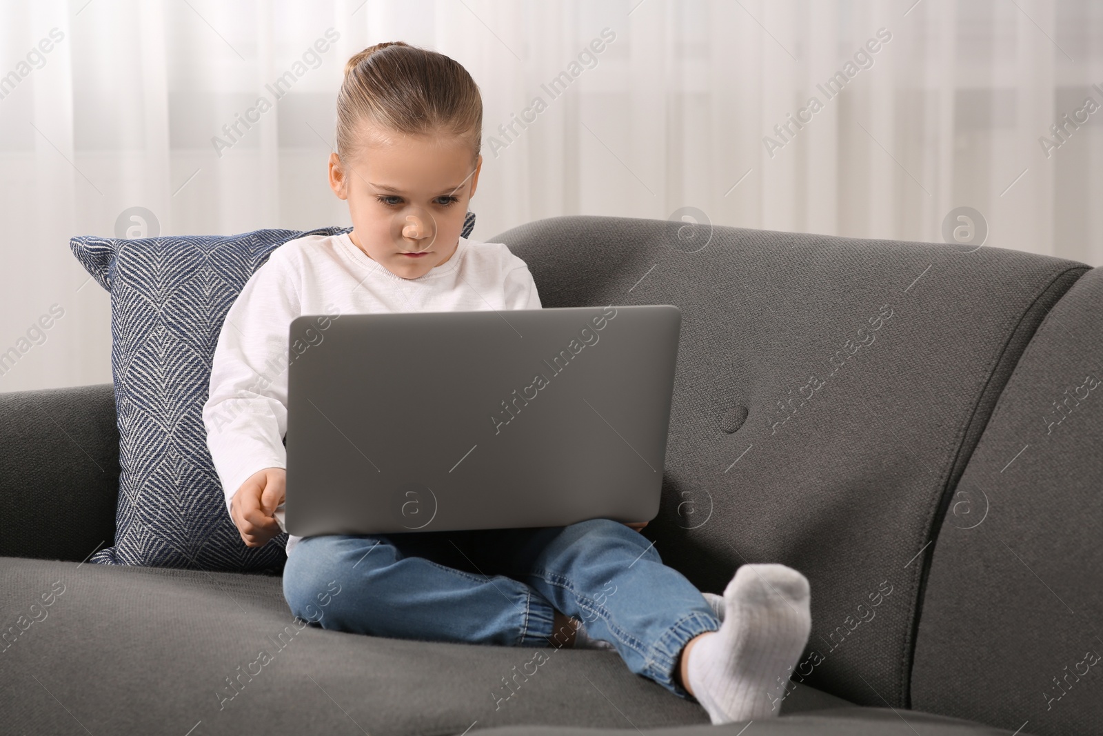 Photo of Little girl using laptop on sofa at home. Internet addiction