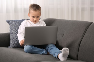 Little girl using laptop on sofa at home. Internet addiction