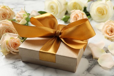 Photo of Golden gift box and beautiful roses on white marble table