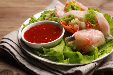 Tasty spring rolls served with lettuce and sauce on wooden table, closeup