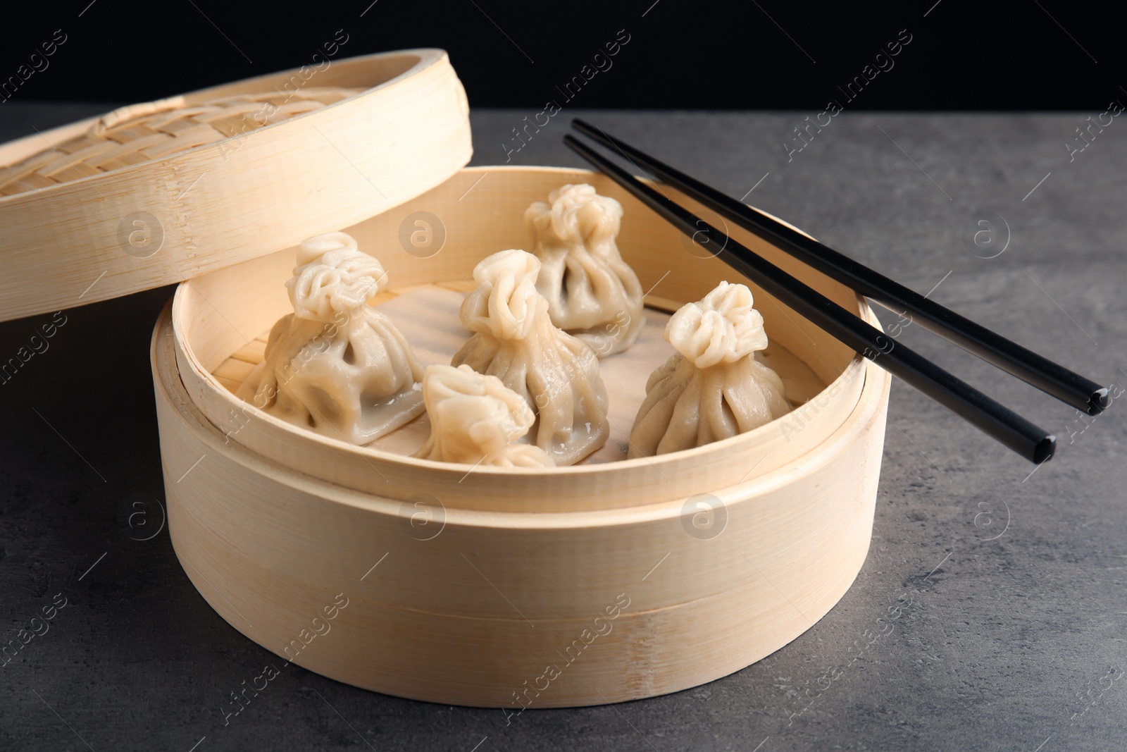 Photo of Bamboo steamer with tasty baozi dumplings and chopsticks on table