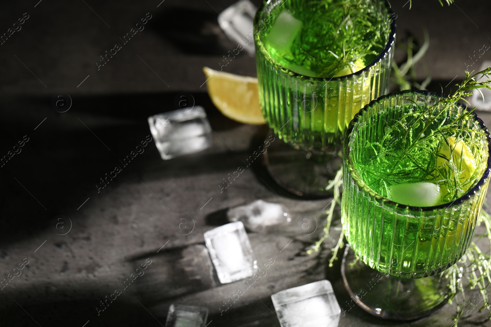 Photo of Glasses of homemade refreshing tarragon drink, ice cubes and sprigs on grey table, space for text