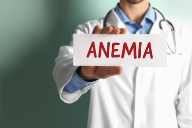 Image of Doctor holding sign with word ANEMIA on color background, closeup