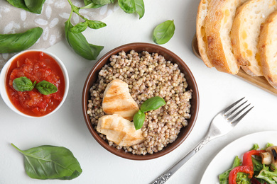 Tasty buckwheat porridge with meat on white table, flat lay