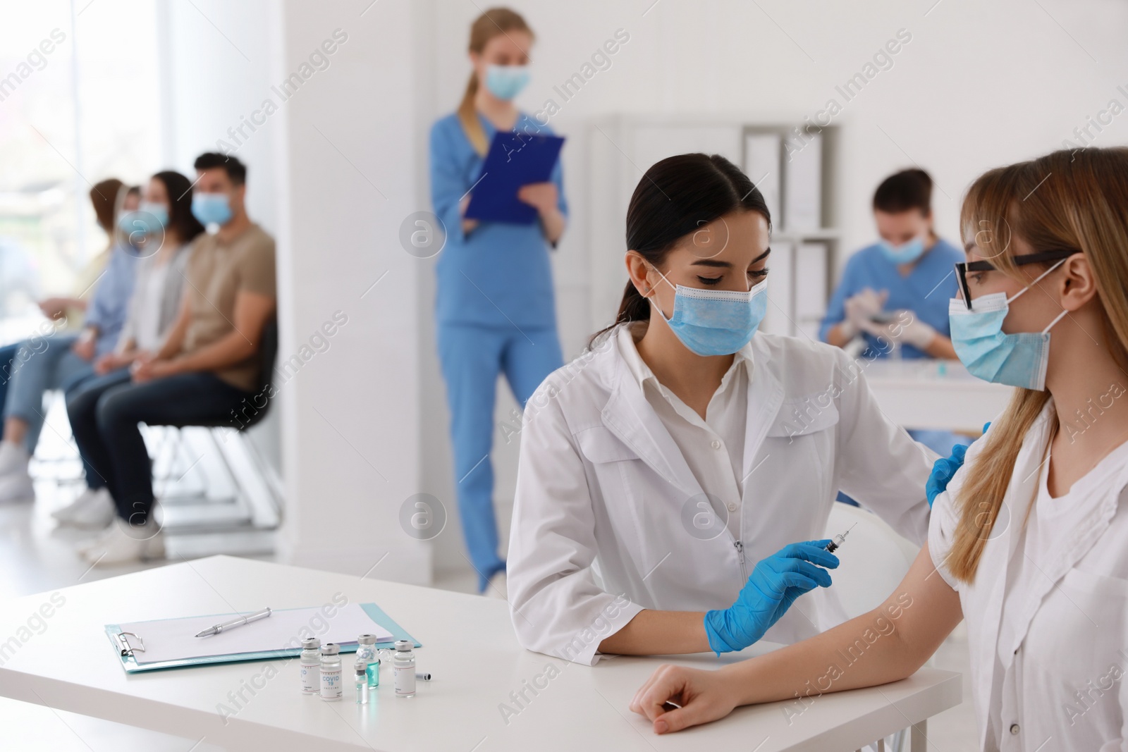 Photo of Doctor giving injection to patient while other waiting in line at hospital. Vaccination campaign