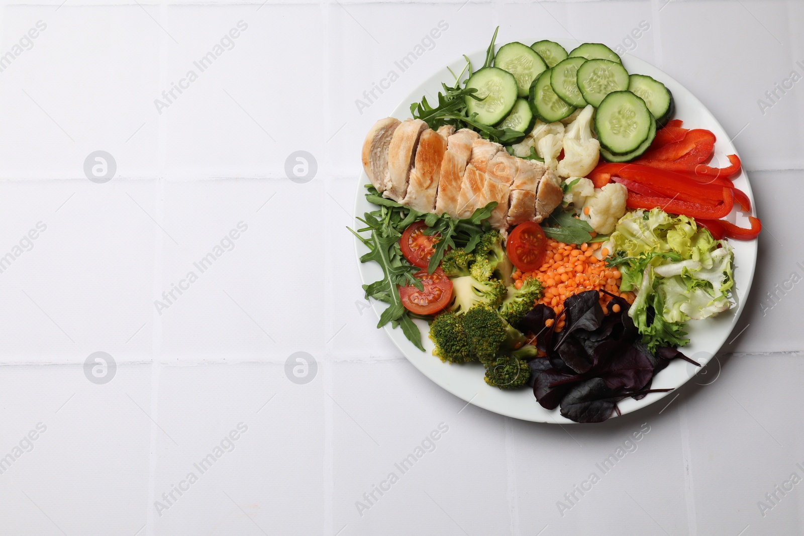 Photo of Balanced diet and healthy foods. Plate with different delicious products on white tiled table, top view. Space for text