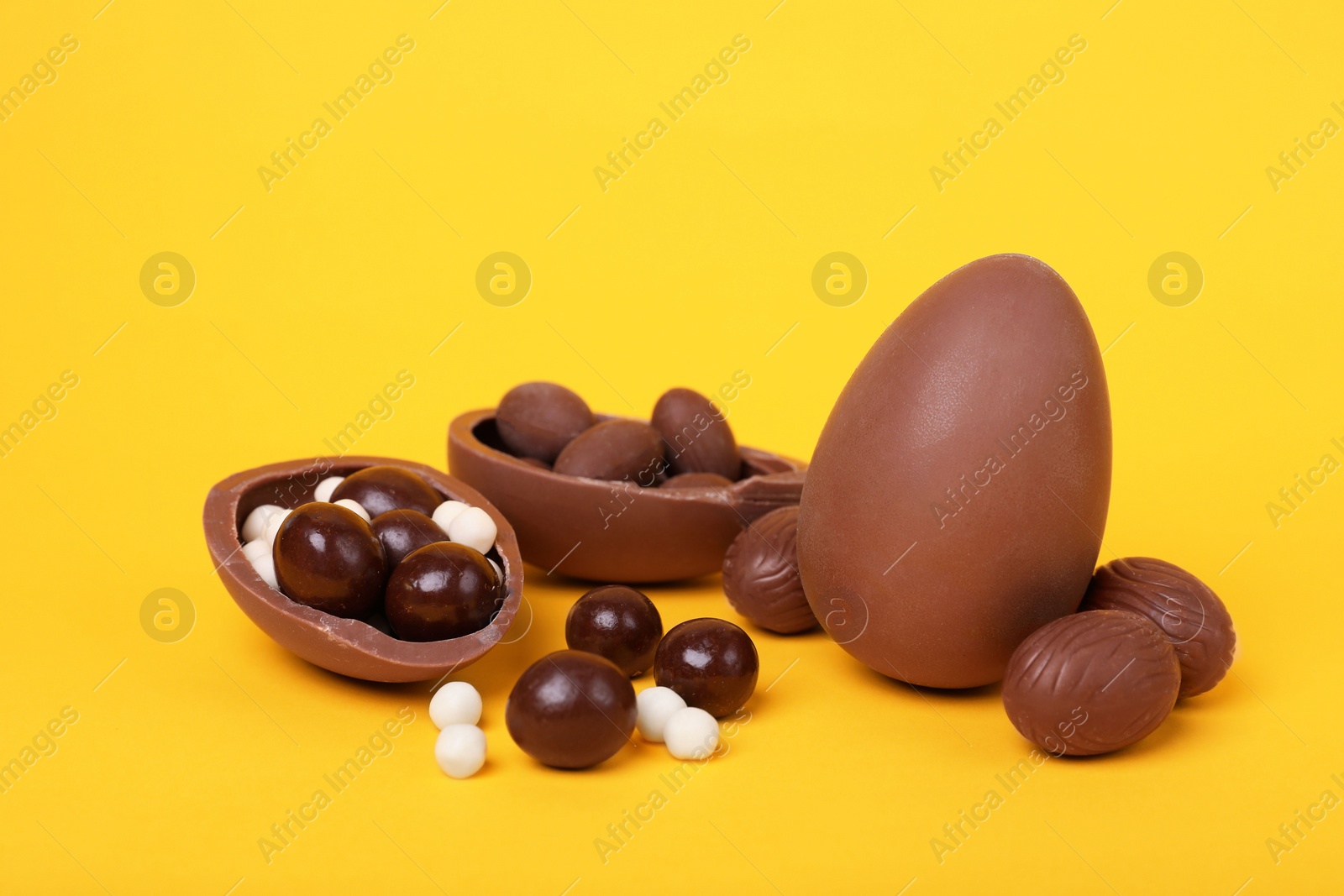 Photo of Delicious chocolate eggs and candies on yellow background, closeup