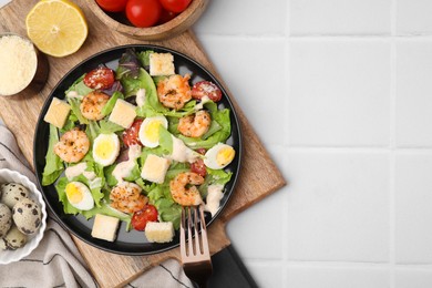 Photo of Delicious Caesar salad with shrimps and fork served on white tiled table, flat lay. Space for text