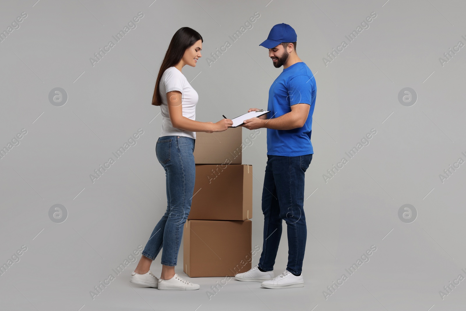 Photo of Smiling woman signing order receipt on grey background. Courier delivery