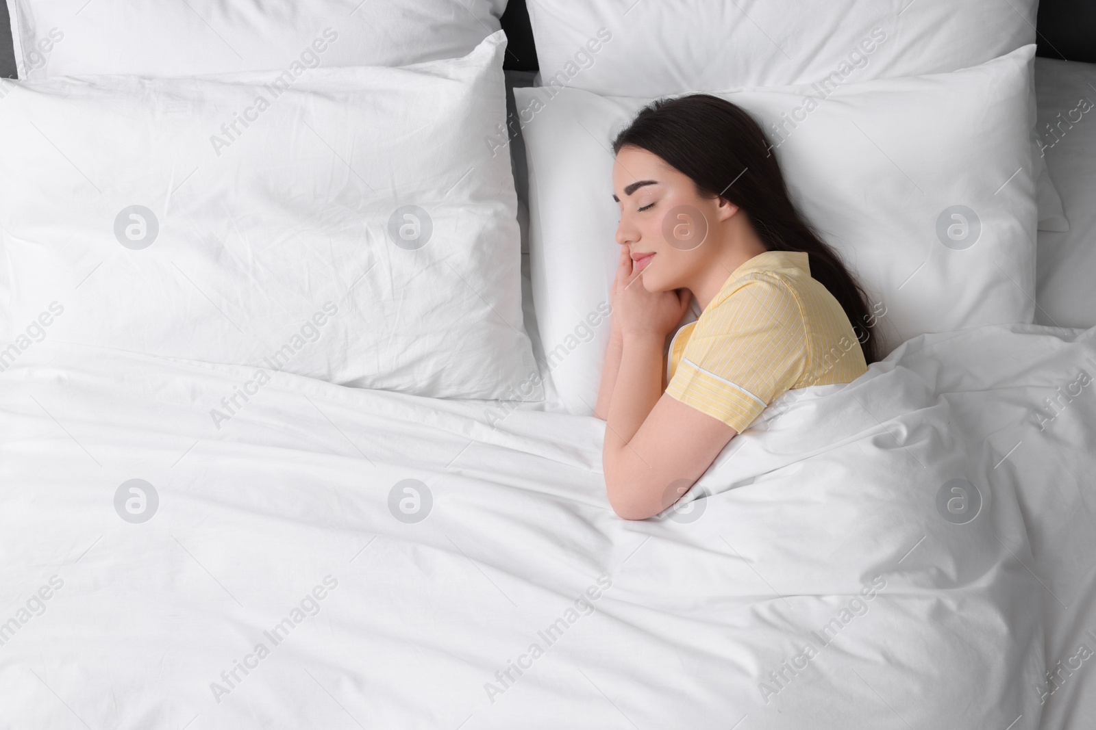 Photo of Beautiful young woman sleeping in soft bed, top view