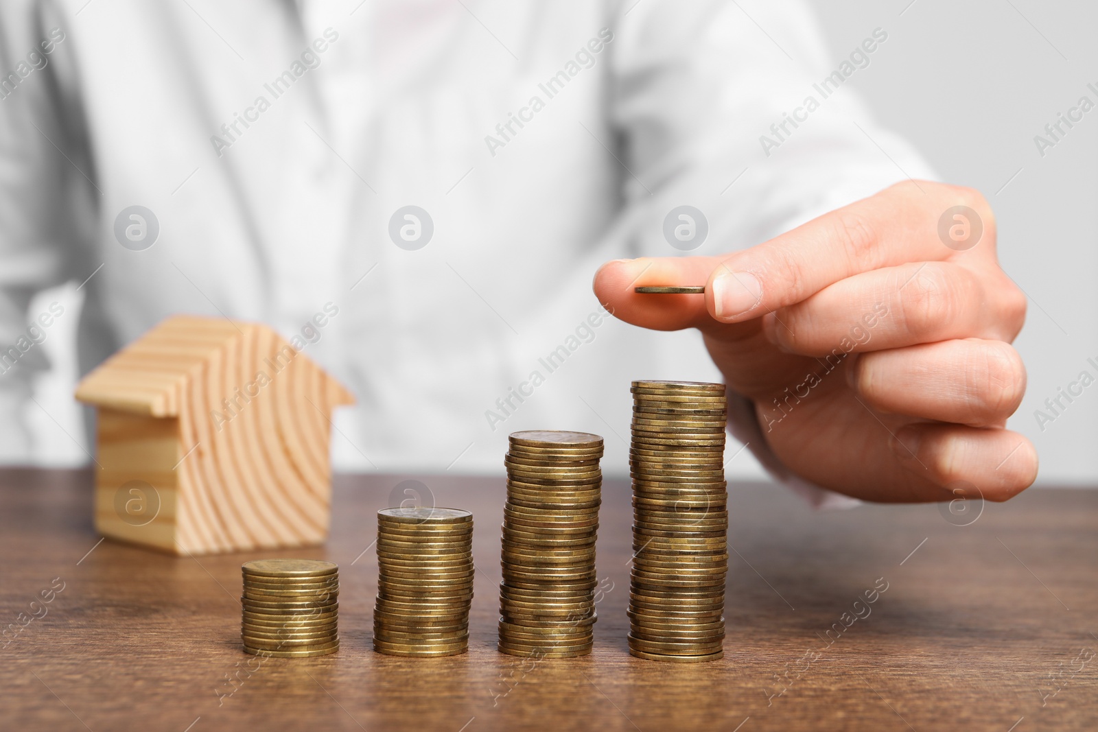 Photo of Mortgage concept. Woman stacking coins near house model at wooden table, closeup