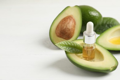 Photo of Essential oil and avocados on white table. Space for text