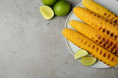 Photo of Plate of grilled corn cobs and limes on grey table, flat lay. Space for text