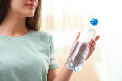 Photo of Woman with bottle of fresh water indoors, closeup