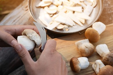 Photo of Man cutting mushroom with knife at wooden table, closeup