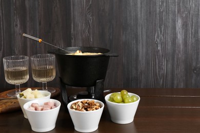 Photo of Fondue pot with tasty melted cheese, forks, wine and different snacks on wooden table, space for text
