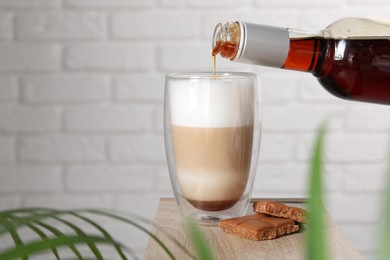 Pouring syrup into glass of tasty coffee on wooden table