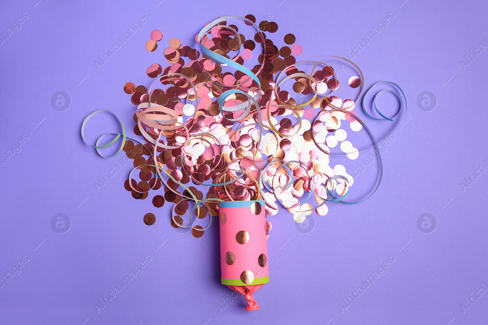 Photo of Bright confetti and serpentine bursting out of party popper on violet background, flat lay