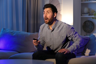 Surprised man watching TV on sofa at home, space for text